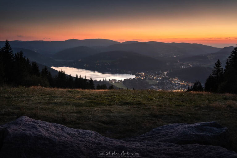Blick vom Hochfirst auf den Titisee bei Abenddämmerung mit aufleuchtenden Tallichtern