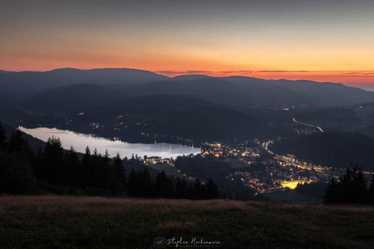 Blick vom Hochfirst auf den Titisee bei Abenddämmerung mit aufleuchtenden Tallichtern