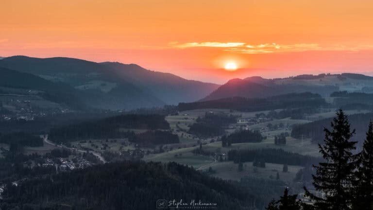Sonne über der Bergkante bei Teleaufnahme im Schwarzwald, sanfte Hügel und goldener Himmel