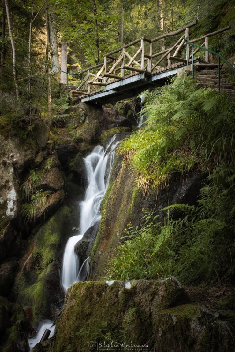 Gertelbach-Wasserfall im Schwarzwald am Abstieg mit Holzbrücke und moosbedeckten Felsen