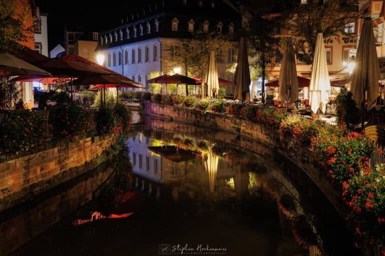 Altstadt von Saarburg bei Nacht mit Blumenkästen, warmen Lichtern und Spiegelung im Wasser