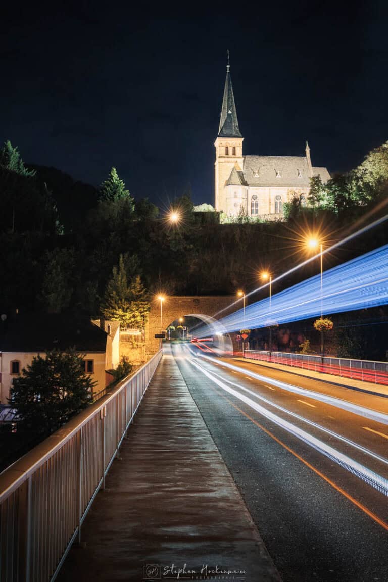 Lichtspuren von Autos auf einer Brücke in Saarburg bei Nacht mit beleuchteter Kirche im Hintergrund
