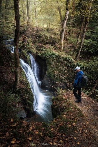 Person blickt von oben auf den Wasserfall bei Maria Martental mit Brücke im Wald